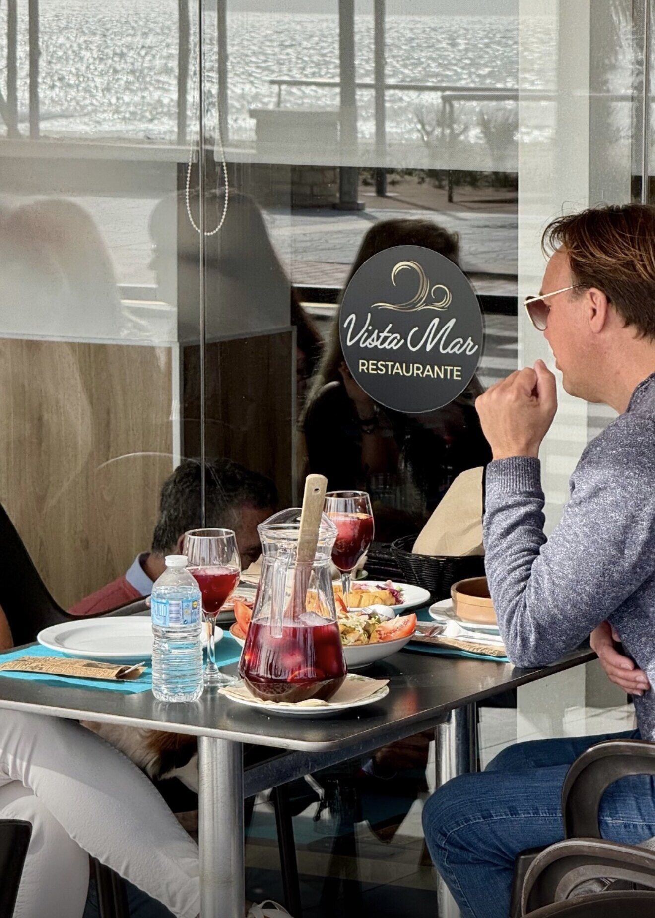 Clientes con una jarra de sangría junto a la cristalera, con el mar al fondo